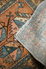 Worn geometric pile of vintage Heriz rug folded, revealing its original selvage and woven foundation.