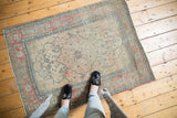 Antique Kerman rug corner, showcasing faded red border, navy floral vinery, and light tatter.