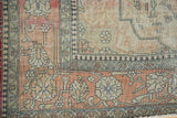 Corner of antique Kerman rug: faded cochineal field, elegant floral vinery, and detailed ivory border.