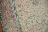 Antique Kerman rug showing faded cochineal red border, ivory field, navy designs, and visible wear.