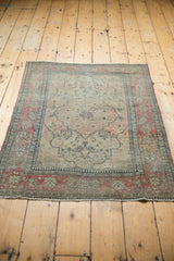 Antique Kerman rug's faded cochineal raspberry floral border, navy outline, and tattered end.