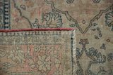 Antique Kerman rug corner: hand-knotted foundation beneath faded raspberry red and ivory pile.