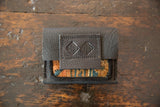 Dark leather flap with stitched embossed logo over a colorful rug fragment.