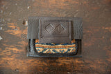 Dark brown leather flap with embossed logo, showcasing geometric rug fragment in blue and beige.
