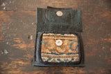 Open leather coin purse reveals patterned tan, blue, orange rug fragment and metal snap.
