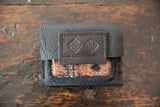 Embossed geometric logo on the stitched dark brown leather flap of the coin purse.