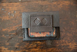 Dark brown pebbled leather flap with a logo over a colorful woven rug fragment.