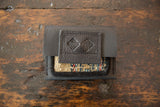 Embossed logo and colorful woven rug fragment on dark leather coin purse.