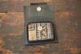 Open leather coin purse with geometric rug fragment in beige, blue, red; metal snaps.