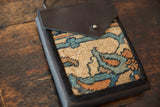 Textured dark leather flap with a snap closure against the coarse weave of a rug fragment bag.