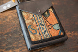 Dark leather trim stitched around the woven orange and blue rug fragment corner.