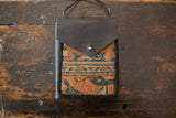 Textured weave of the bag's rug fragment in orange, blue, and beige geometric patterns.