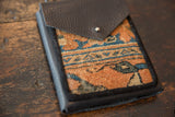 Textured dark leather flap with a metal snap over a geometric orange and blue rug fragment.