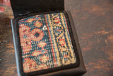 Teal, red, and beige patterned rug fragment on leather shoulder bag, featuring a metal snap.
