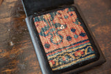 Hand-woven rug fragment with unique geometric pattern, metal snap, and dark leather edge.