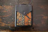 Dark leather shoulder bag with distinctive orange, blue, and beige rug fragment, metal snap.