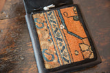 Textured orange and blue geometric rug fragment on shoulder bag with metal snap.