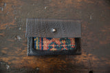 Rug fragment wallet with textured black leather flap open over a colorful woven panel.