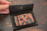 Interior view of a black leather wallet showing a colorful rug fragment pocket with a snap.