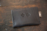 Embossed geometric logo on the dark, pebbled vegetable-tanned leather wallet.