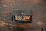 Black leather Dainty Wallet partially open, revealing patterned blue and tan rug fragment.
