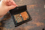 Hand holding open rug fragment wallet, revealing patterned orange, blue textile and silver snap.