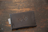 Dark brown vegetable tanned leather wallet featuring embossed geometric logos and visible stitching.