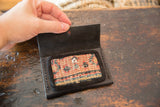 Black leather Dainty Wallet open, showing geometric terracotta and blue rug fragment.