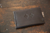 Dark brown leather back of the Dainty Rug Fragment Wallet with embossed geometric logos.