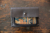 Dark leather wallet flap with silver snap, revealing colorful woven rug fragment.