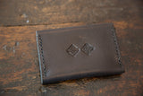 Wallet back showing dark brown textured leather, embossed geometric logos, and hand-stitched detail.