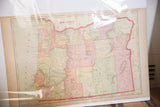 Full 1907 Cram's Oregon map under clear plastic, showing pastel counties from an angle.