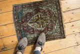 Overhead view of an antique silk Kashan mat with a moody, abrashed palette of eggplant and aqua blue.