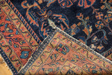 Folded corner of the Lilihan rug, revealing navy floral field, dusty raspberry border, and reverse with light tatter.
