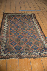Antique Belouch rug detail: terracotta, indigo serrated medallions, wave border, and visible pile wear.