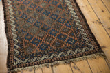 Antique Belouch rug corner, showcasing ivory reciprocating wave border, 'pawn' motif, and tattered fringe.