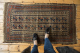 Antique Belouch runner corner detail: geometric motifs in camel, cherry red, indigo, with tattered edge.