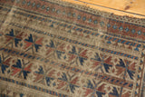Tattered edge and visible pile wear of an antique Belouch rug, with geometric patterns in indigo, red, and camel.
