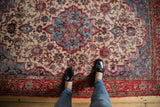 Distressed Persian Meshed rug detail: even wear on ivory field with red floral tendrils.