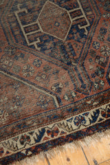 Shiraz rug corner: madder red and indigo geometric patterns, worn pile, tattered fringe.