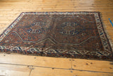 Vintage Shiraz rug corner, madder red and indigo geometric patterns, tattered ivory fringe.