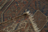 Vintage Shiraz rug corner detail, highlighting madder red, indigo geometric motifs, and tattered fringe.