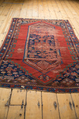Geometric indigo blue border, cherry red field, and visible wear on an antique Caucasian rug.