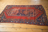 Antique Caucasian rug detail: cherry red field, geometric indigo border, and aged hand-knotted texture.