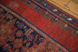 Antique Caucasian rug detail showing cherry red field, indigo blue border, geometric motifs, and characteristic wear.