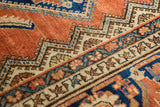 Terracotta field with navy, ivory serrated patterns, and floral details on a vintage rug.
