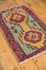 Distressed Oushak rug corner showing aubergine, gold, and green geometric motifs and short fringe.