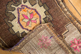 Folded vintage Oushak rug corner revealing distressed chocolate pile, bright pink motif, and hand-knotted back.