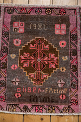 Distressed Oushak rug close-up: 1982 weaver inscription, blush fuchsia, and charcoal motifs.