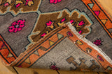 Distressed Oushak rug corner revealing vivid fuchsia motifs, orange border, and fringed edge.